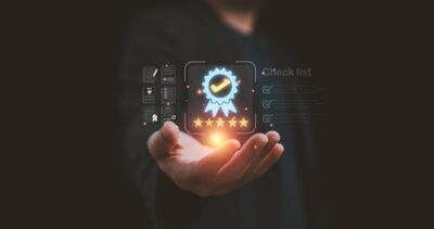 Image of a hand that holds a glowing digital badge with a checkmark, stars, and checklist icons floating above it.