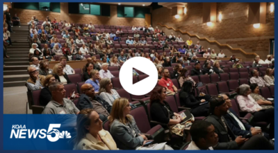 Screenshot of a KOAA News5 video showing a large audience seated in a tiered auditorium at the PPBEA Regional Careers Pathway Summit. Attendees of varied ages and backgrounds sit in rows of purple seats, facing forward toward an unseen speaker. A play button icon appears centered on the image, and the KOAA News5 logo is visible in the corner.